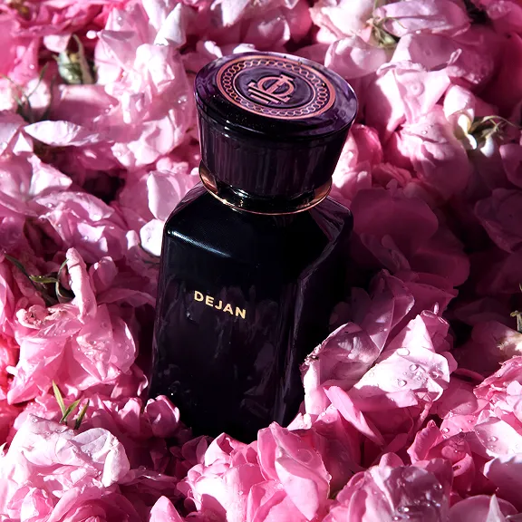 Parfümflakon DEJAN: dunkel, eingebettet in leuchtend rosa Rosenblätter.